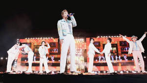 K-pop團體在夜晚燈光舞台上表演同步舞蹈動作。