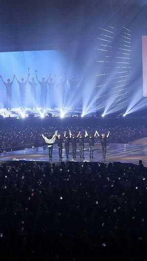 K-pop表演者在舞台上高舉雙臂，在明亮的燈光下被歡呼的粉絲包圍。