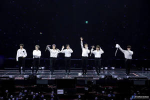 七位K-pop偶像在燈光璀璨的舞台上表演，背景是星空，粉絲們在歡呼。