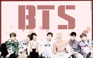 七位K-pop偶像在一個巨大的粉紅色BTS標誌下，與裝飾氣泡一起擺姿勢。