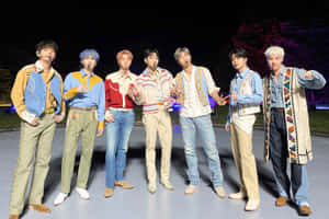 七位男性表演者穿著協調的服裝在夜間舞台上擺姿勢。