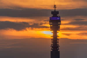 BT 塔在帶有雲朵的鮮豔橙色日落天空下呈現剪影。 — 倫敦 壁紙