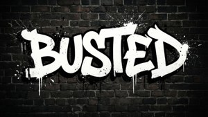 深色磚牆上帶有油漆飛濺和滴落的白色塗鴉單詞 busted