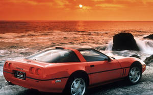橙色Corvette停泊在岩石海灘，背後有海浪和日落。