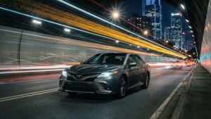 灰色轎車在明亮的隧道中快速行駛，模糊的城市燈光掠過。