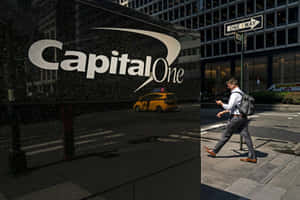 男子在人行道上走過 Capital One 大樓，帶有黃色的士倒影。
