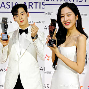 兩位身穿白色服裝的獎項得主在Asia Artist Awards活動中手持獎盃擺姿勢。