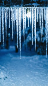 在雪夜中，溫暖的燈泡照亮了從屋頂垂下的冰柱。