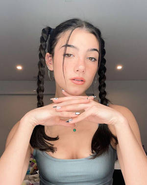 年輕女性，辮子頭髮，戴著圓環耳環，在室內雙手合十靠近下巴擺姿勢。