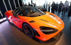 橙色McLaren超級跑車展出，人們在現代展廳中觀看。 — Steam Deck 壁紙