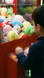 小孩玩夾娃娃機遊戲，裡面有色彩繽紛的毛絨玩具