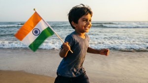一個微笑的男孩在日落時分拿著印度國旗在海灘上奔跑。