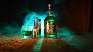 Chivas Regal 18酒瓶和Red Bull罐在帶有紋理的表面上，散發青綠色光芒和煙霧。