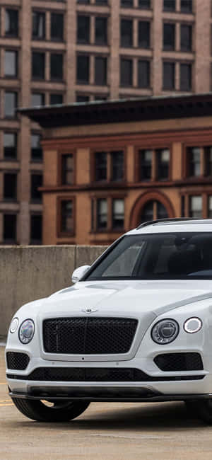 白色賓利Bentayga SUV停泊在磚砌建築附近的城市街道上。 — iPhone 14 壁紙
