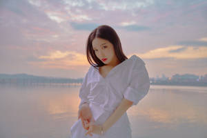 夕陽下穿白色襯衫的女子在水邊，遠處有城市燈光