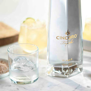 Cincoro Blanco龍舌蘭酒瓶和加冰的杯子放在大理石表面上。