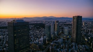 黃昏時分的東京城市景觀，在紫橙色天空下，有發光的摩天大樓和遠山