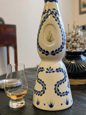 裝飾性藍白陶瓷瓶，帶金色徽章，旁邊是深色桌上的威士忌杯。