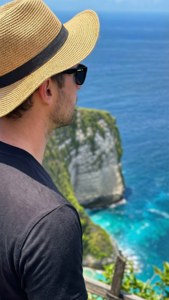 戴草帽和太陽眼鏡的男人從懸崖邊俯瞰碧綠海洋