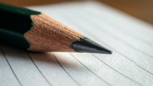 一支削尖的綠色鉛筆筆尖放在橫線紙上，準備書寫。