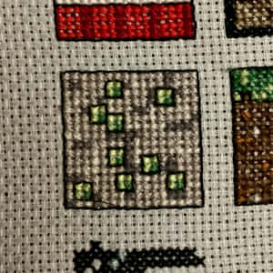 用綠色同紅色線喺布料上十字繡嘅Minecraft方塊。 — iPad 壁紙