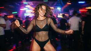 一名女子在色彩繽紛的俱樂部燈光下穿著黑色魚網服裝跳舞。