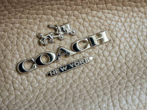 米色皮革上的銀色Coach標誌，帶有馬和馬車。
