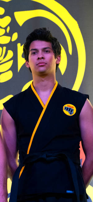 年輕武術家身穿黑色鑲黃邊的服裝在標誌背景前擺姿勢。