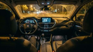 夜間汽車內部，發光儀表板和濕潤擋風玻璃，顯示前方街燈。