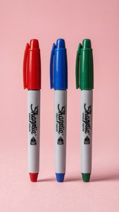 粉紅色背景上的三支Sharpie記號筆（紅色、藍色和綠色）