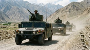 軍用悍馬車載著武裝士兵在泥路上行駛，穿越岩石山脈。