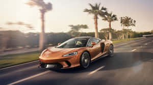 銅色McLaren跑車在日落時分沿著棕櫚樹成蔭的道路疾馳。 — 4K 法拉利 壁紙