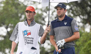 兩名高爾夫球手在雨中行走，一人撐傘，Valero Texas Open