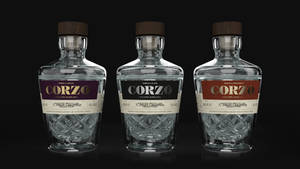 三款帶有不同顏色標籤的Corzo龍舌蘭酒瓶展示在黑色表面上。