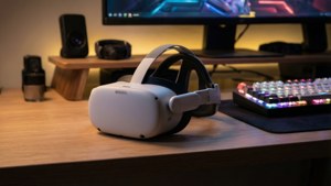白色VR頭戴式裝置在木桌上，配有發光鍵盤和遊戲顯示器。