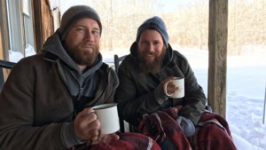 兩個留鬍鬚的男人在積雪的門廊上裹著毯子從杯子裡喝飲料