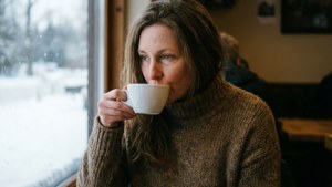 穿棕色毛衣的女性在室內雪窗前喝咖啡