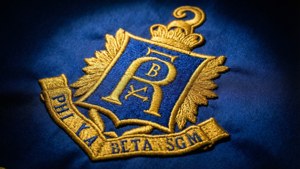 藍色布料上金色刺繡的 Phi Kappa Beta SGM 徽章，帶有月桂葉翅膀和皇冠
