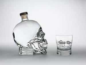 骷髏形狀的酒瓶和裝滿冰塊的杯子放在灰色表面上。