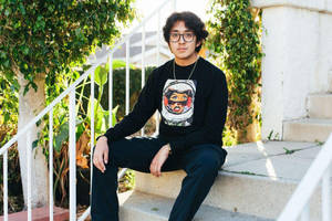 戴眼鏡的年輕男子坐在被綠植環繞的戶外台階上。
