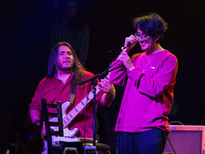 兩位音樂家在紫色燈光下用結他和麥克風在舞台上現場表演。