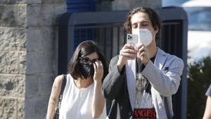 一對戴著口罩的情侶在陽光普照的街道上靠近石牆自拍。 — 浪漫愛情 壁紙