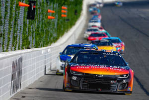 NASCAR 賽車在帶有橙色安全錐和綠色牆壁的賽道上飛馳。