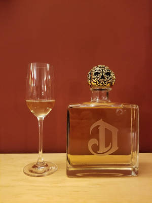 方形玻璃醒酒器，金色蓋子蝕刻D，旁邊香檳笛形杯，木質表面，紅色牆壁背景。