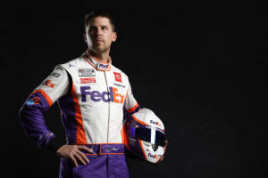 NASCAR車手身穿FedEx賽車服，在黑色背景前手持頭盔。