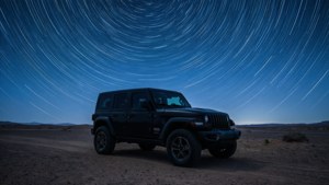 夜間沙漠中，黑色Jeep Wrangler停在星軌下