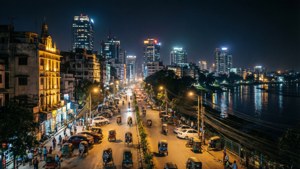 夜間城市街道，有發光的車輛和行人，旁邊是反射的河流。