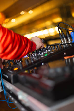 DJ的手在俱樂部溫暖燈光下調整混音器旋鈕。