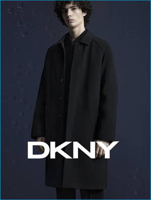 一位穿著黑色外套的模特兒站在帶有水珠和DKNY標誌的藍色牆壁前。