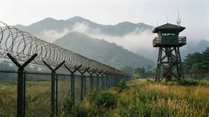 一座木製瞭望塔在鐵絲網圍欄旁，山脈在霧中